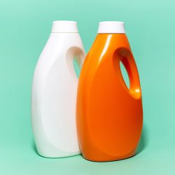 Close-up of two, white and orange, detergent bottles on background of aqua menthe color.